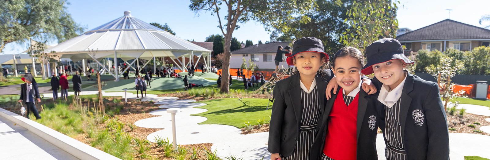 Three primary school students standing in front of a new playground, smiling.