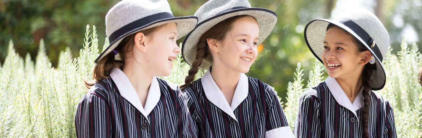 Three students smiling next to a garden bed on the school grounds.