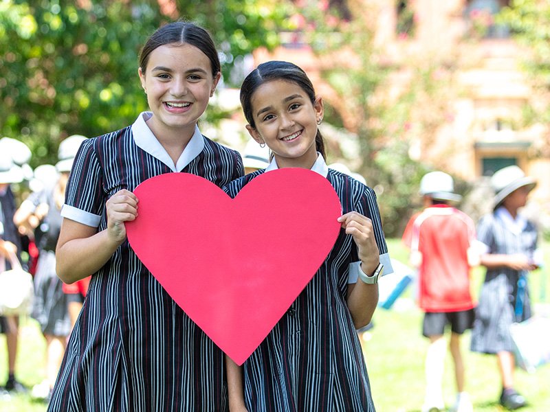 Two students smiling together, holding a large paper heart cutout.