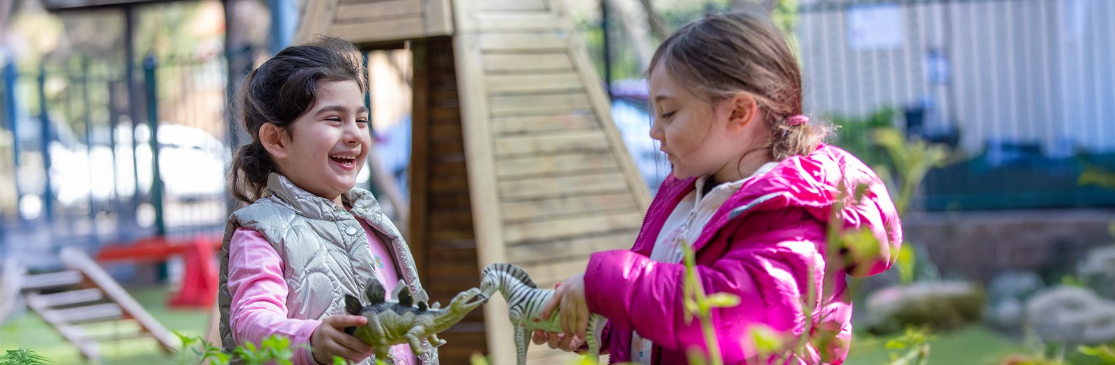 Two kindergarten children playing with toy animals outside in the playground.