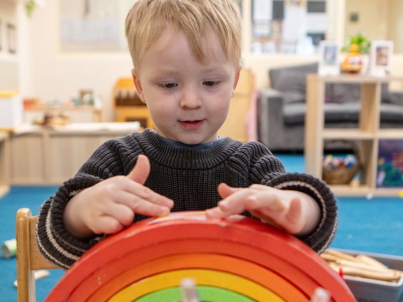Child in a classroom playing with a wooden rainbow toy.
