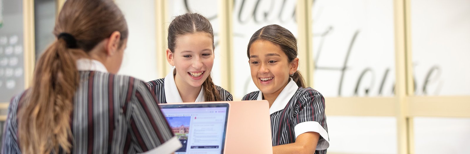 Three students smiling and working together on laptops.