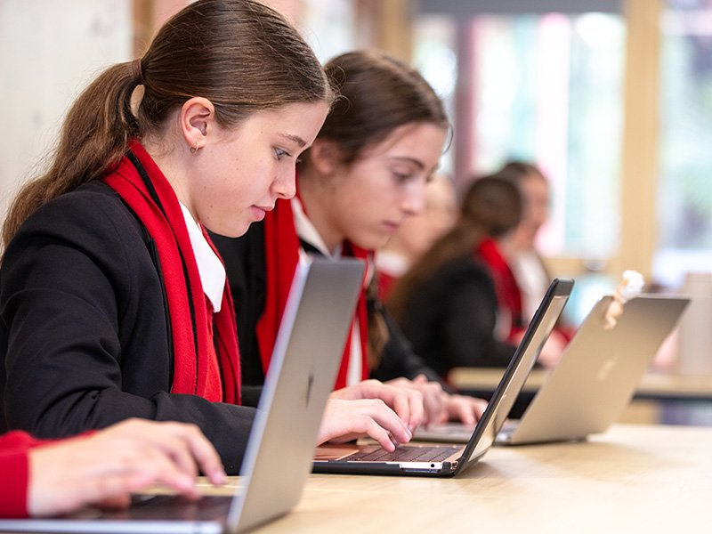 Row of high school students in class, focused on their work on laptops.