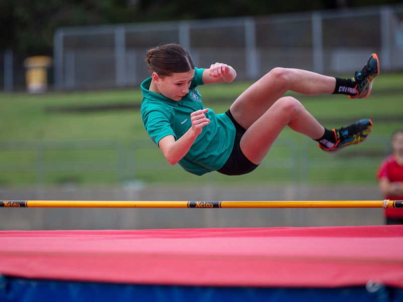 Student leaping over a high jump hurdle onto a mat.
