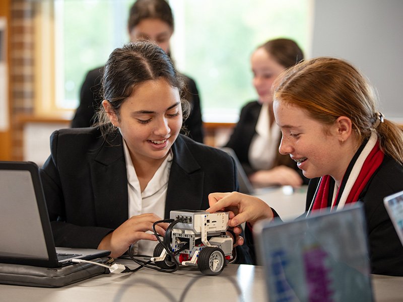 Two high school students smiling while constructing a robot in class.