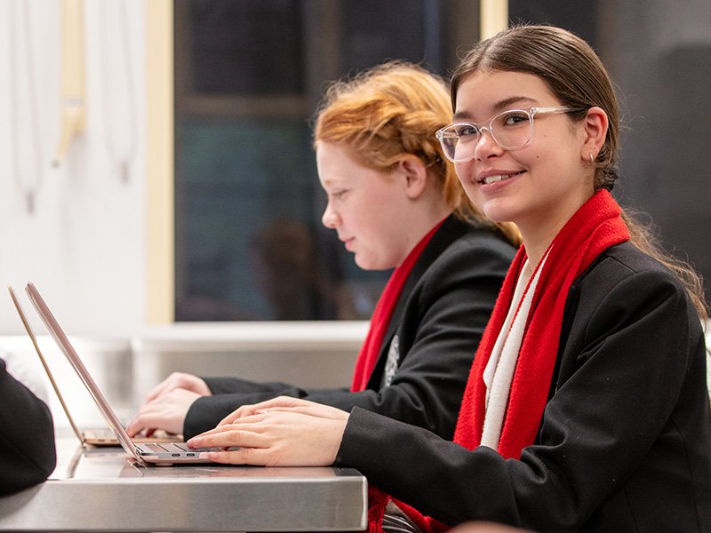 Two students typing on laptops during class.