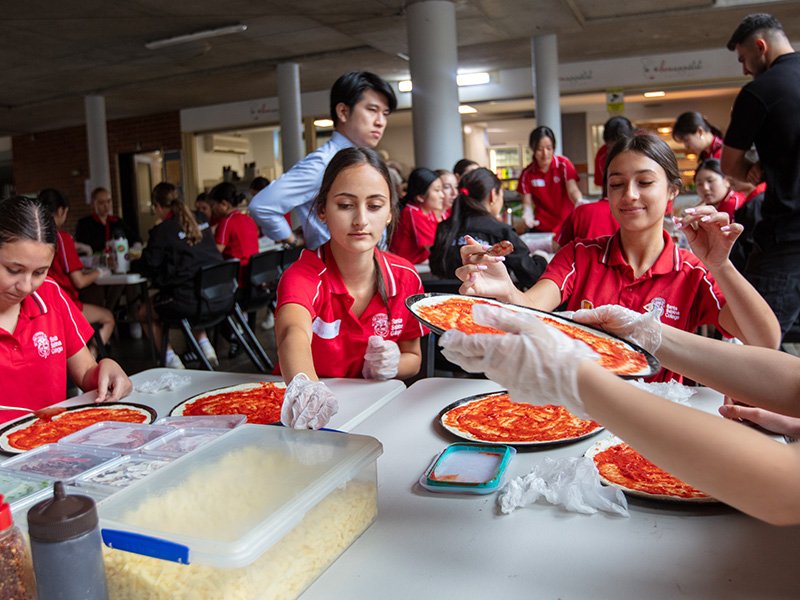 Students sitting together in house colour groups, making pizza.