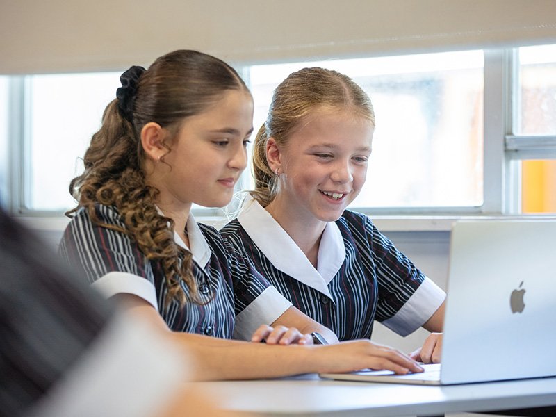 Two high school students working together on a laptop in class.