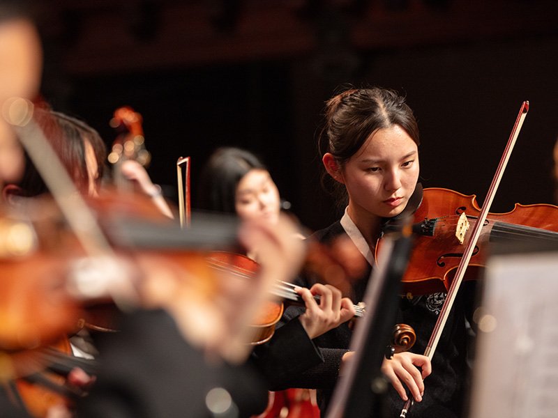 Students playing string instruments in the orchestra.