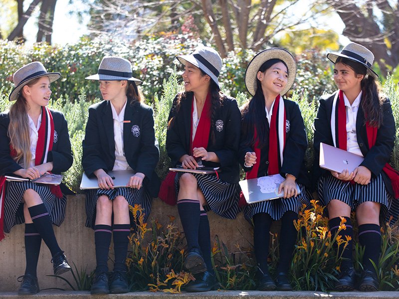 Five high school students sitting together, talking on a garden bench.