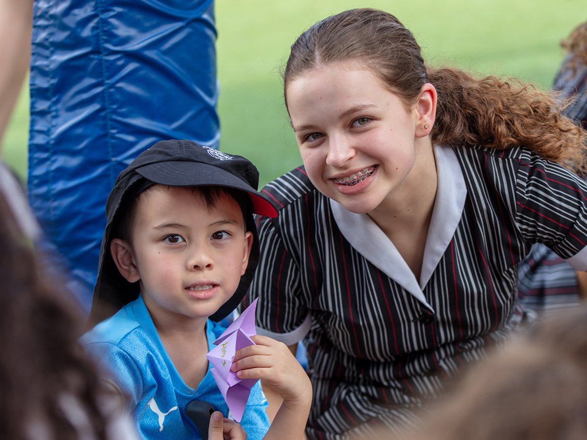 A high school student smiling with a primary student holding origami.