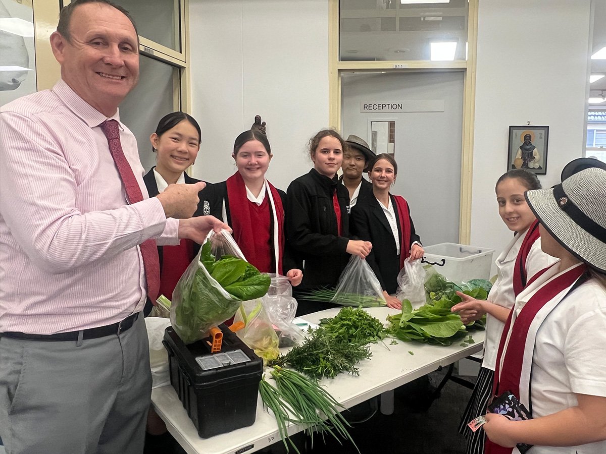 A group of students holding fresh produce in class, smiling with their teacher.