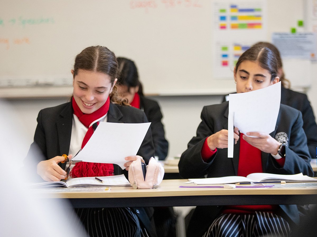 Two students in the classroom, cutting paper for their workbook.