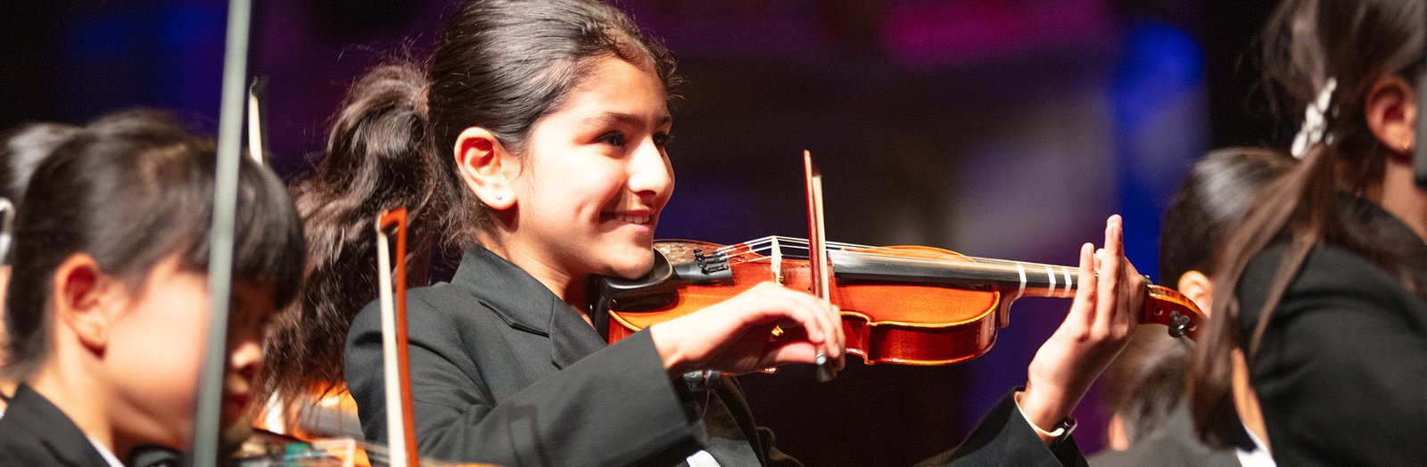 Student smiling while playing a string instrument in the orchestra.