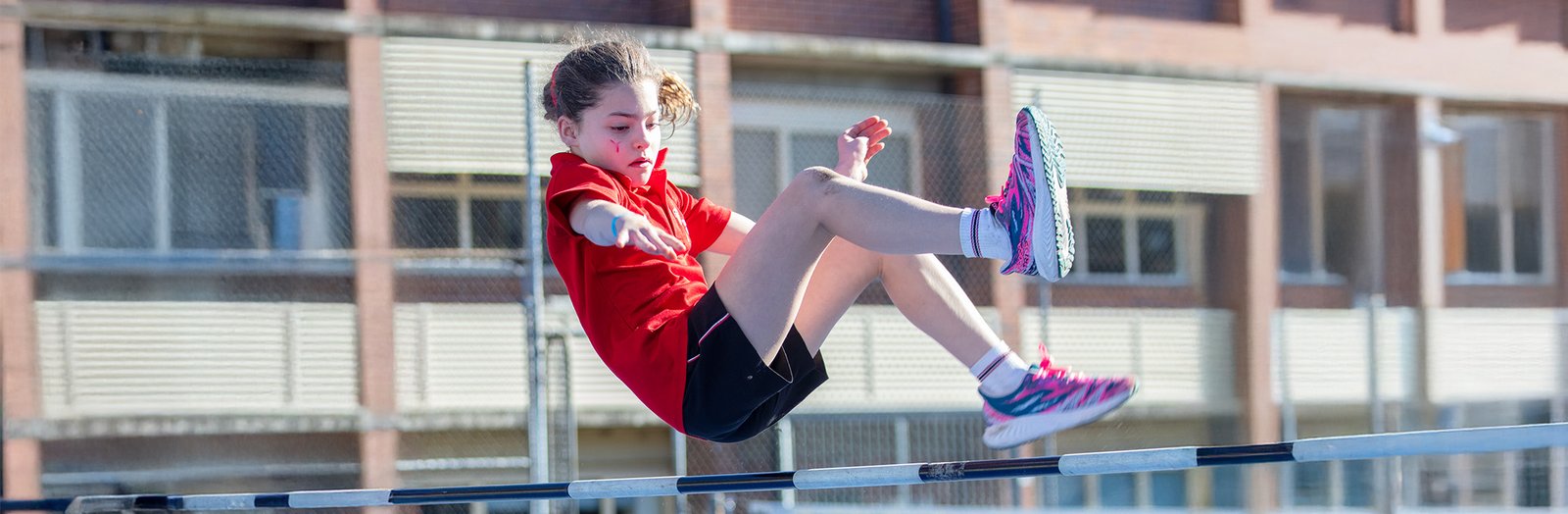 Primary student dressed in house colours, doing high jump.