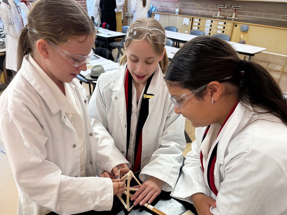 Three students working on a science project, wearing lab coats and safety goggles.