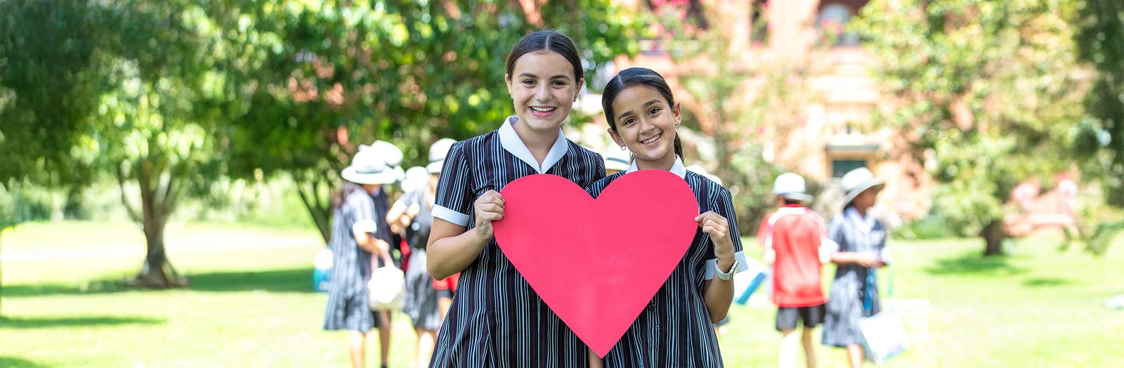 Two students smiling while holding a large paper cutout heart.