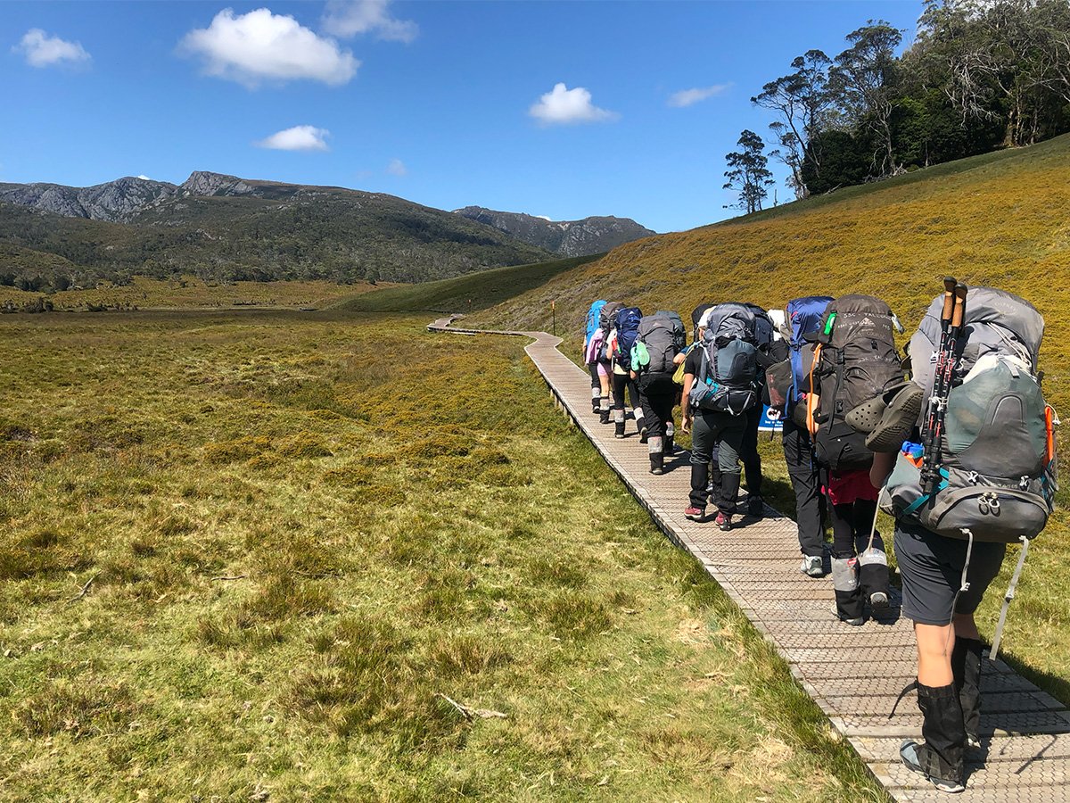 Students hiking on a boardwalk through bushland, carrying hiking packs.